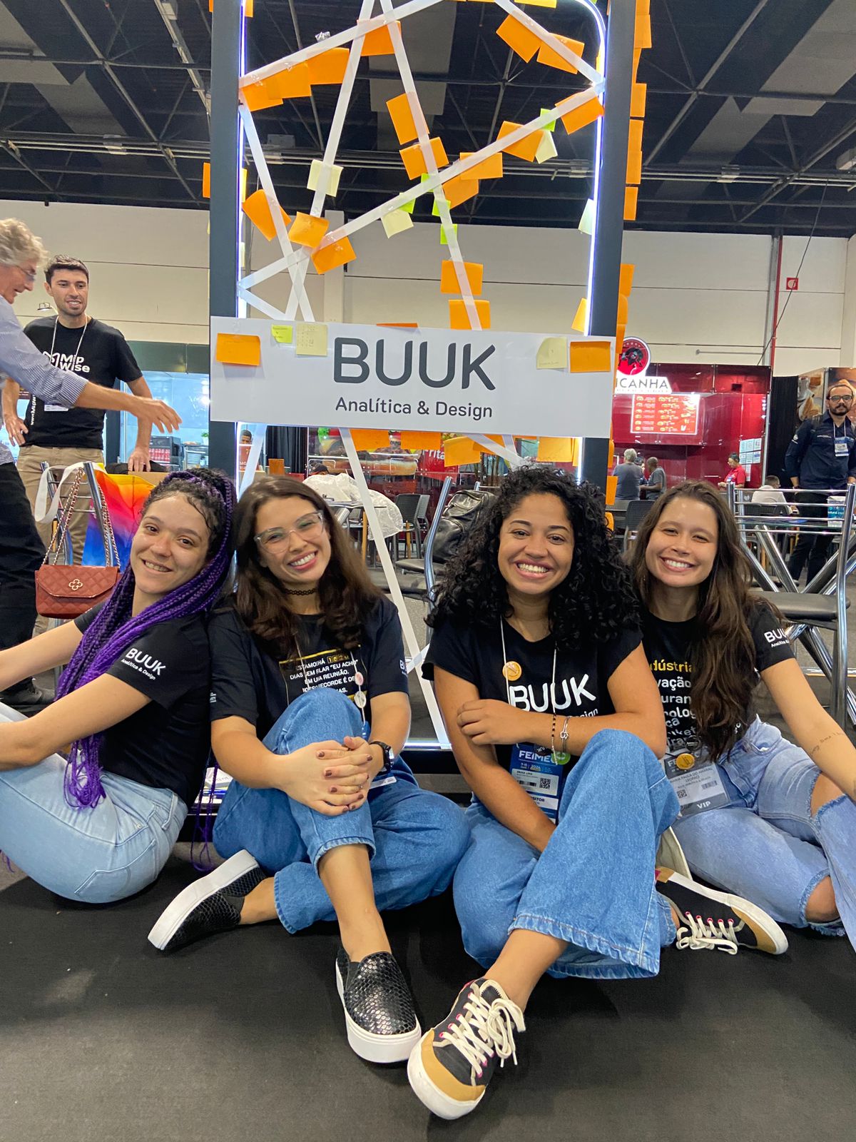 Aurilene Candida, Ravine Gonçalves, Érika Lima e Maria Paula no estande da Buuk Analítica e Design durante a Feira Internacional de Máquinas e Equipamentos, Feimec, em São Paulo Expo. O painel com o logotipo da Buuk está repleto de post-its que remetem aos visitantes no espaço durante a feira.